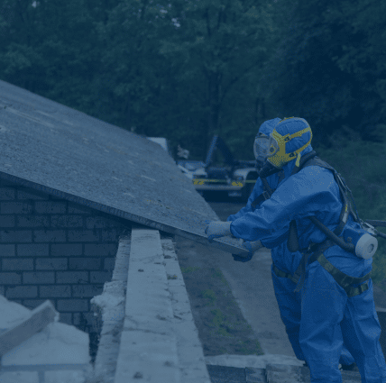 Worker in protective gear touching roof shingle containing asbestos