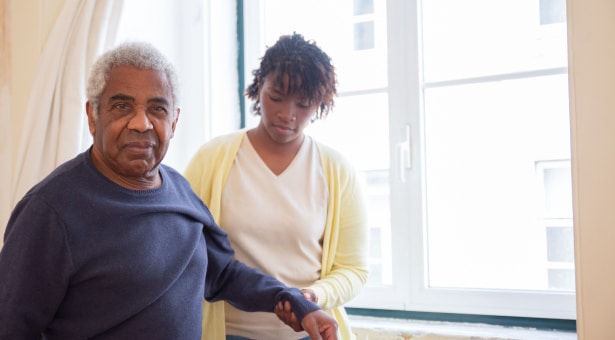 Younger female aiding older man getting dressed