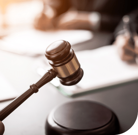 Wooden gavel about to strike, with lawyers writing in the background.