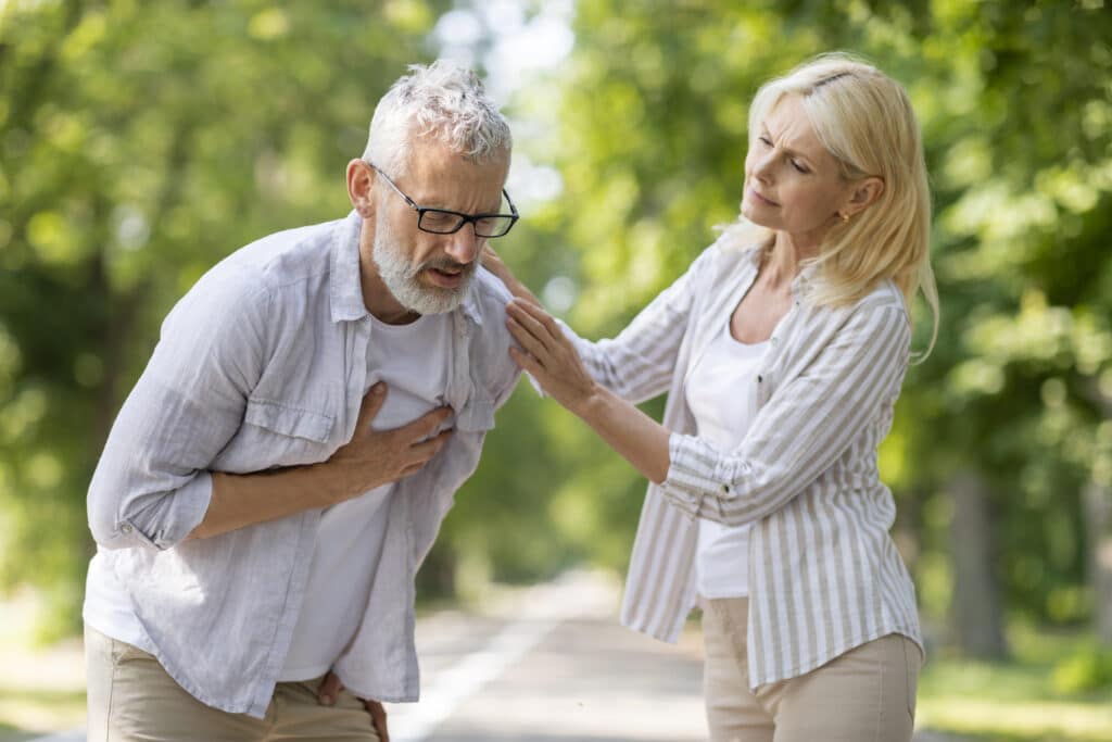 Mature man experiencing sudden chest pain while walking with his wife in a park.