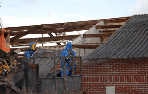 Workers wearing protective equipment removing asbestos-containing roof from an old building
