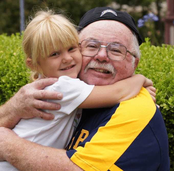 Grandpa with sports shirt and cap hugging young granddaughter