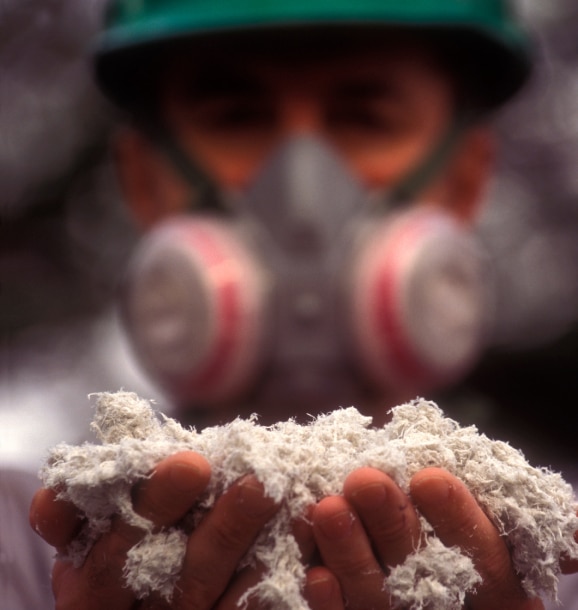 Man wearing protective equipment and holding a handful of asbestos fibers with both hands