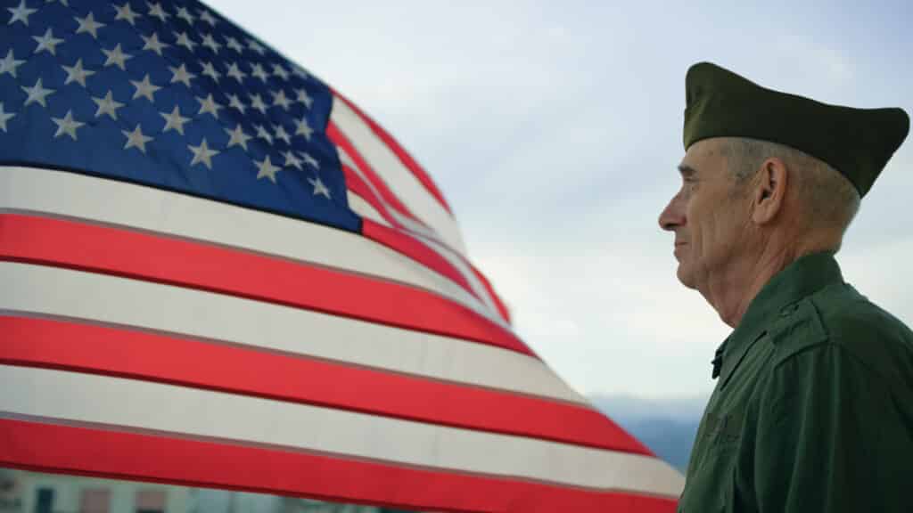 Elderly veteran with mesothelioma looking at the horizon with a U.S. flag waving in the back