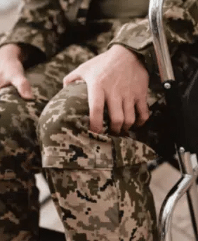 Person in military uniform in wheelchair holding their legs