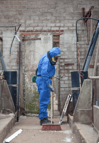 Worker with protective equipment sweeping asbestos from the floor in a toxic exposure site