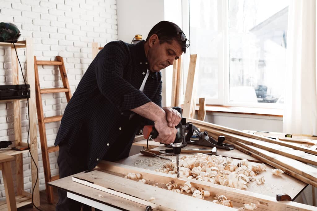A carpenter drilling into a wooden plank, unaware that the timber may be contaminated with asbestos