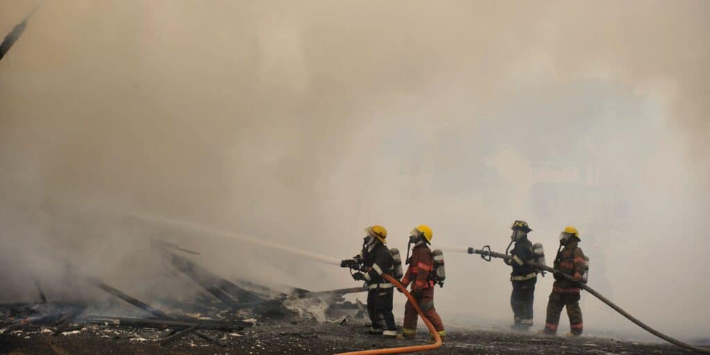First responders inside a cloud of heavy smoke and debris after a building collapse risking asbestos exposure