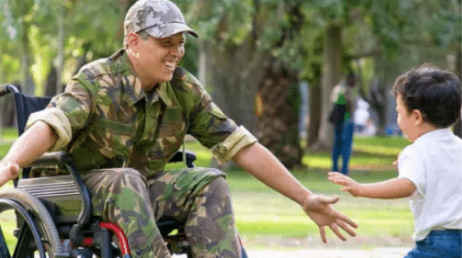 Man in army uniform in wheelchair greeting young boy