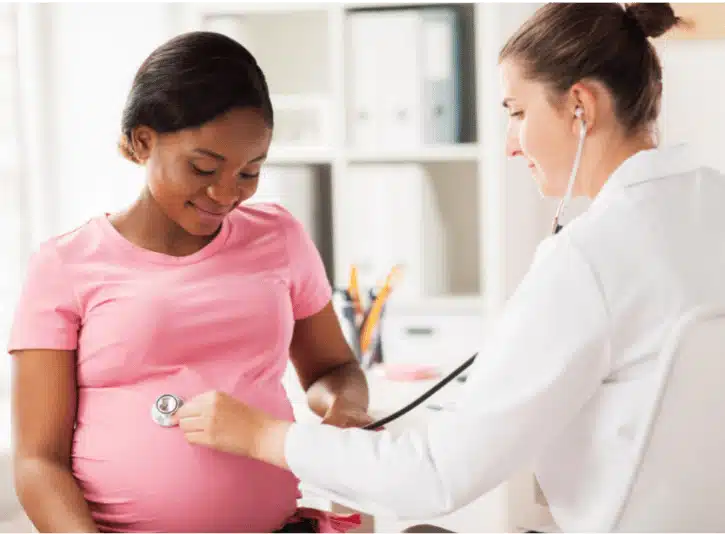 Doctor listening to fetal heartbeat with stethoscope on expectant mother’s abdomen