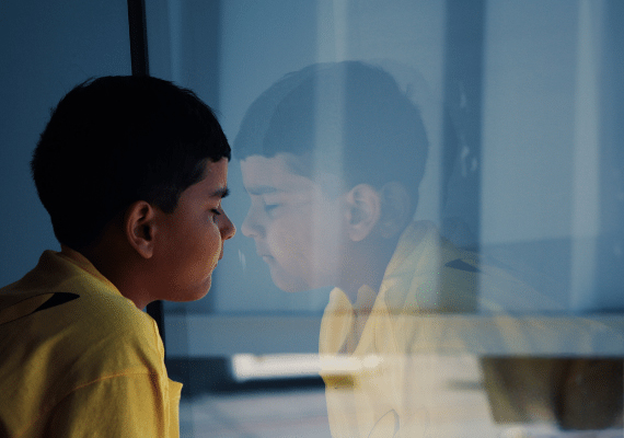 Worried child with head against a window