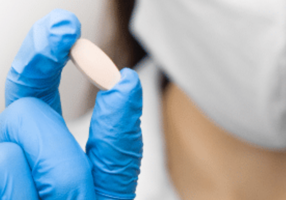 Doctor with a gloved hand holding a pill