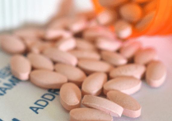 Pink pills falling from an orange prescription bottle