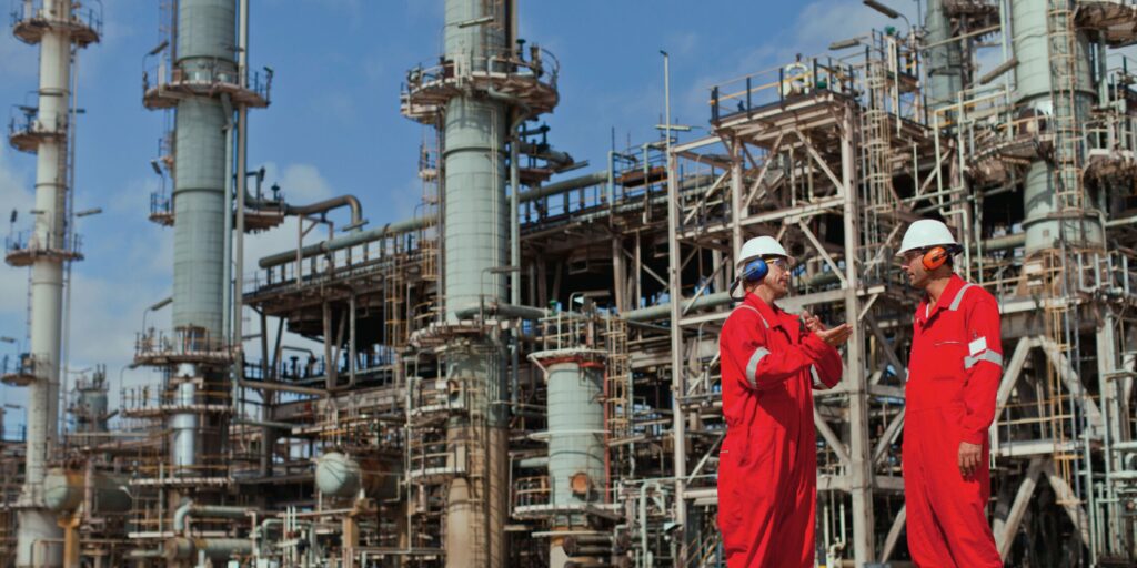 Oil refinery workers talking, wearing a red suit, but without masks to protect them against potential asbestos exposure
