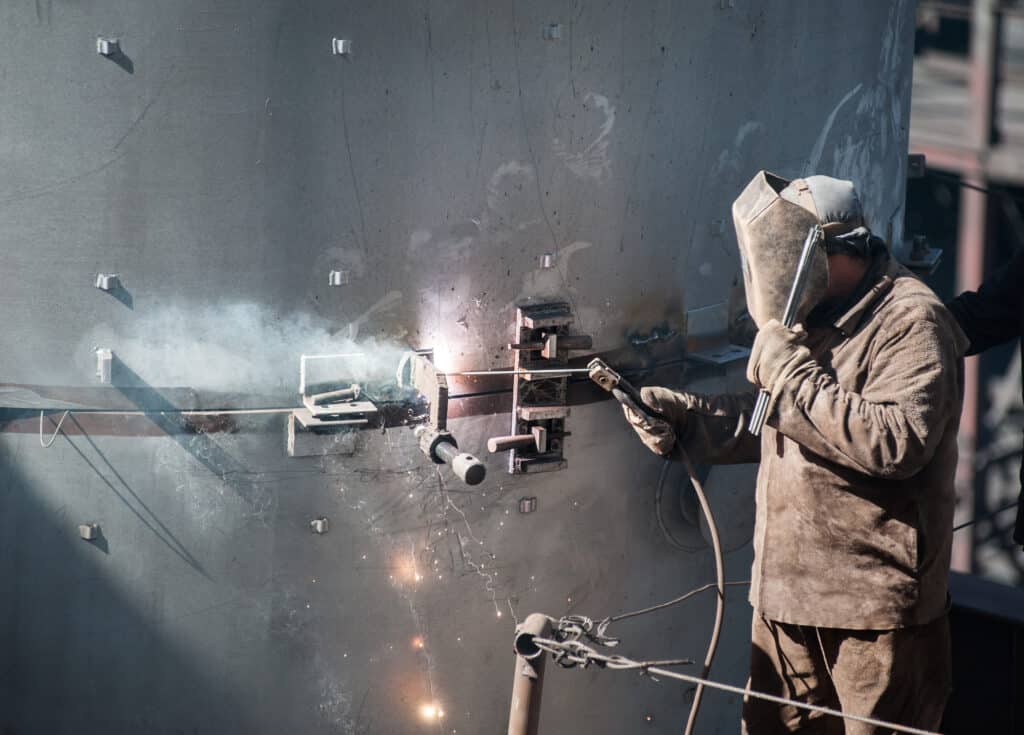 Worker doing industrial welding job outdoors protecting against sparks but without mask to protect against asbestos exposure