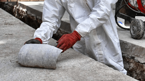 Person with protective equipment removing asbestos from the floor