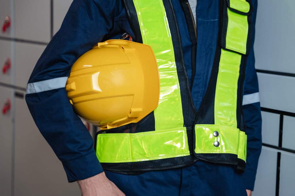 A person in a dark blue uniform and safety vest is holding a yellow hard hat.
